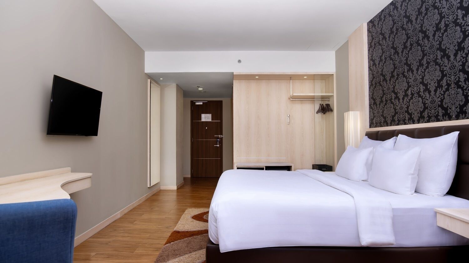 A hotel room with a bed, a flat-screen TV, a wooden wardrobe, and a bathroom visible through an open door.