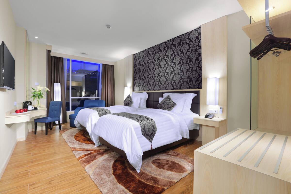 A modern hotel room with a large bed, a desk with a chair, a TV, and a window with curtains.