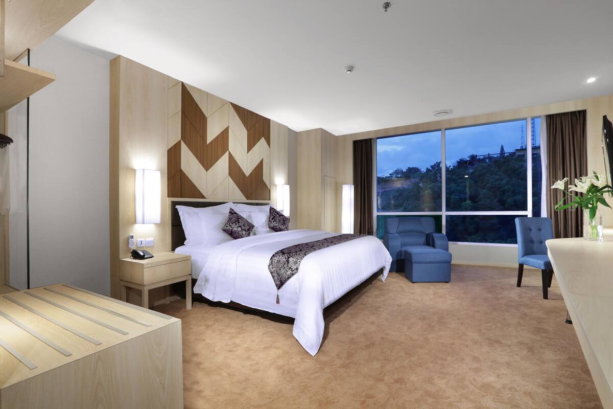 A modern hotel room with a large bed, a desk, and a view of the cityscape.