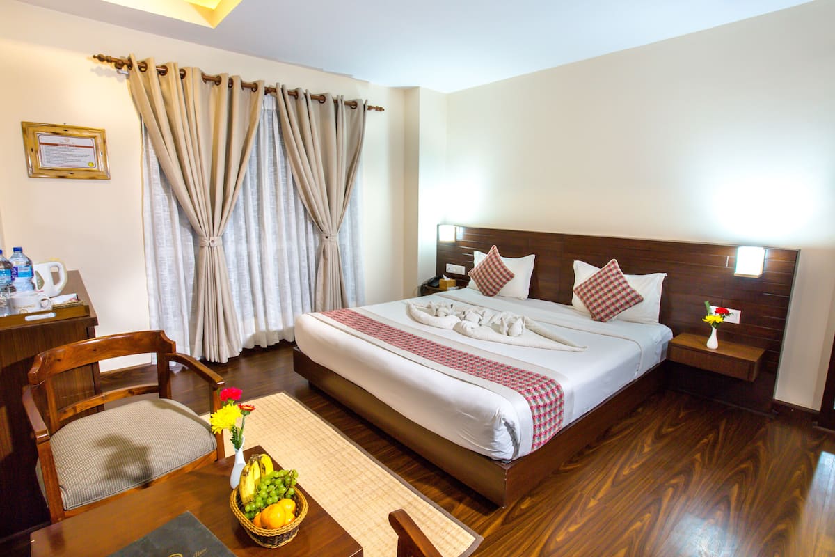 A hotel room with a wooden bed, a desk with a chair, a bedside table with a vase of flowers, and a fruit basket on the table.