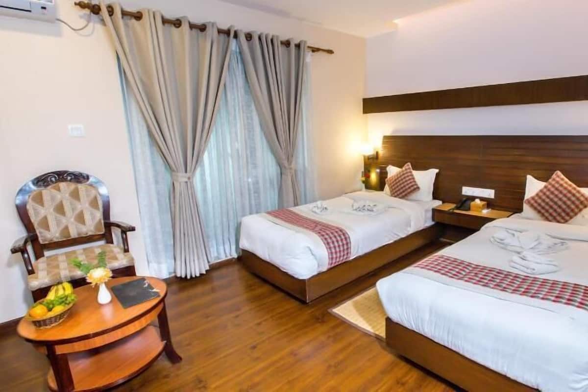 A hotel room with two beds, a wooden chair, a small table with fruit, and a window with curtains.