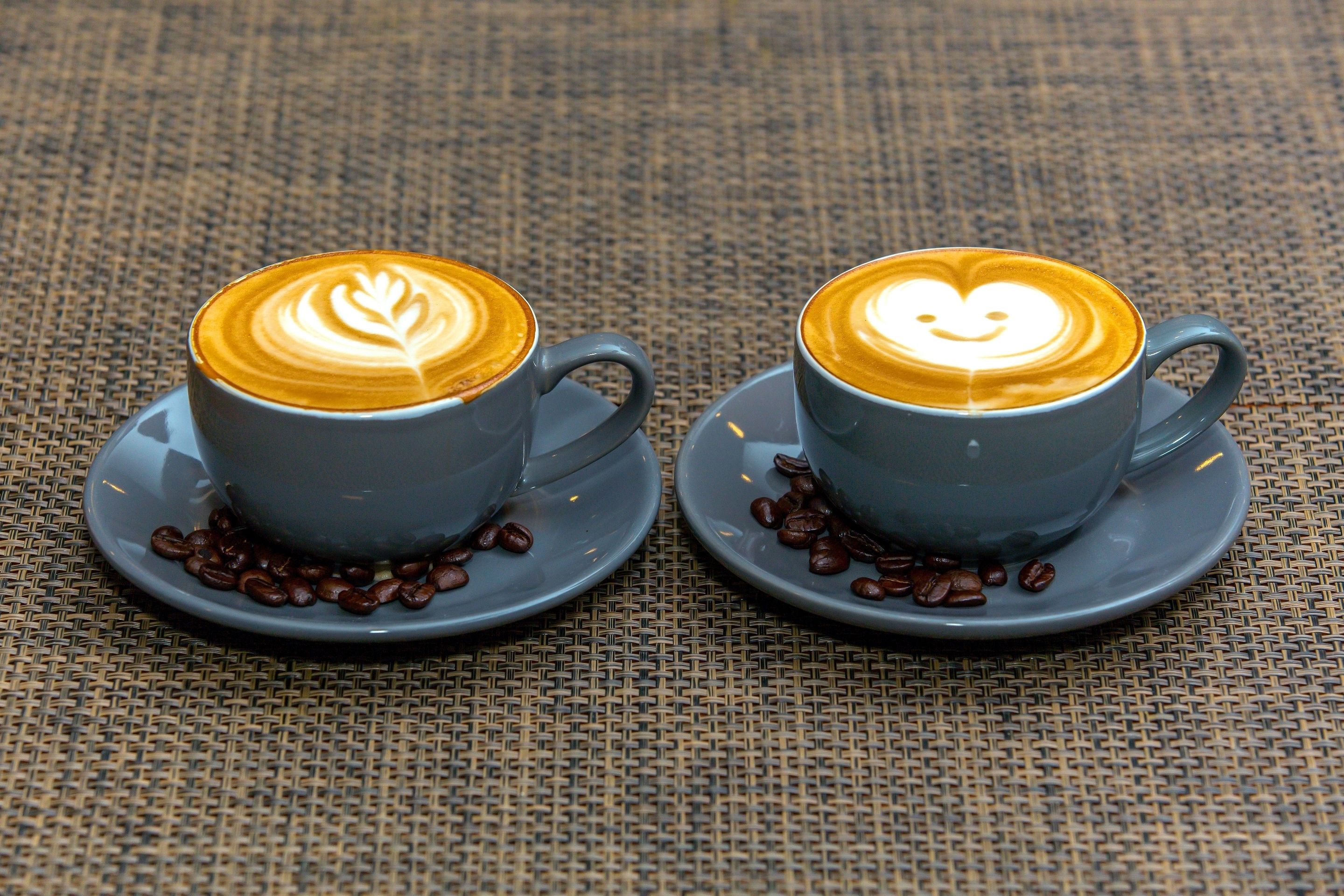 Deux tasses de café décorées de motifs en latte, posées sur une nappe tissée.