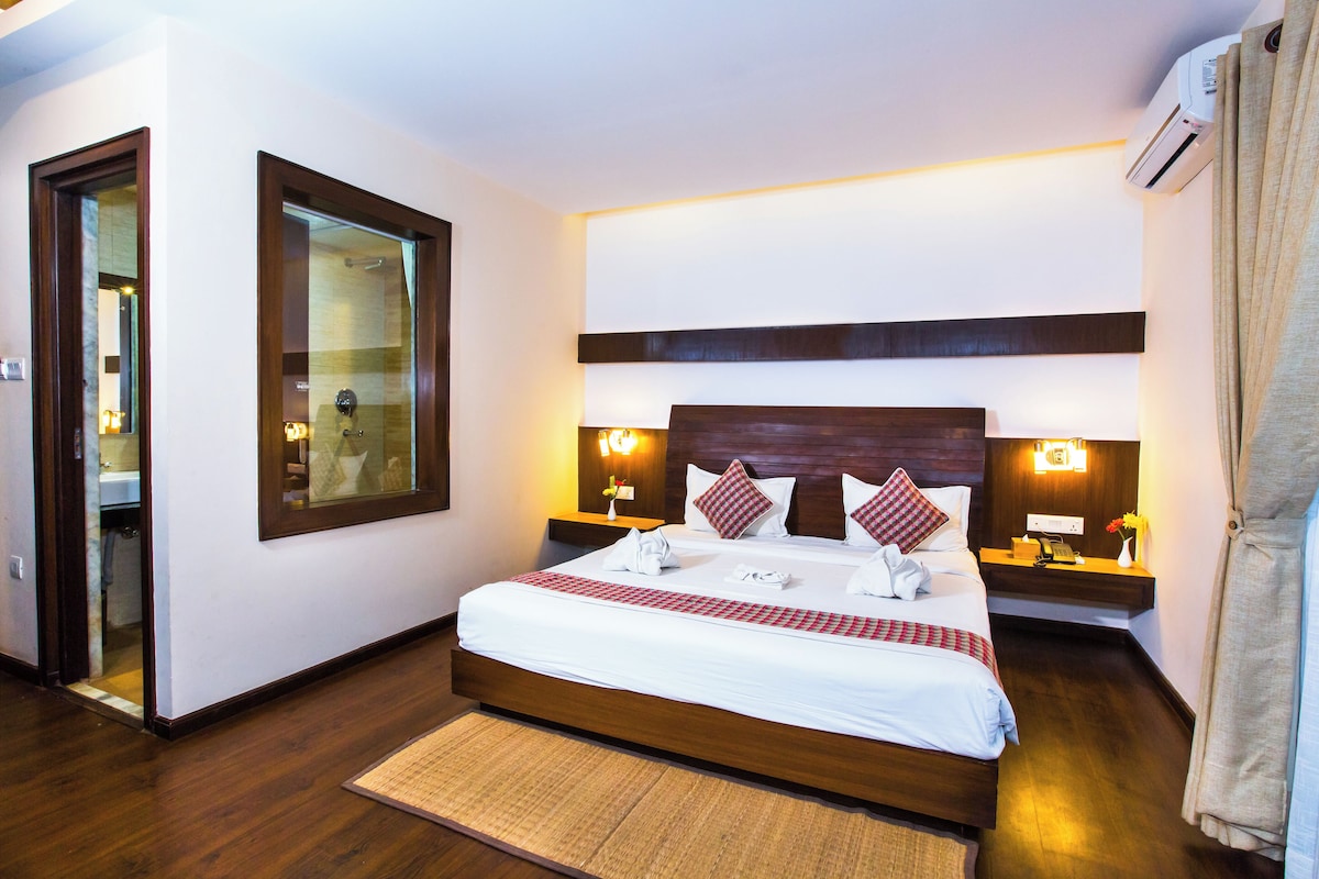 Habitación de hotel con una cama grande, mesitas de noche, un espejo, un equipo de aire acondicionado y piso de madera.
