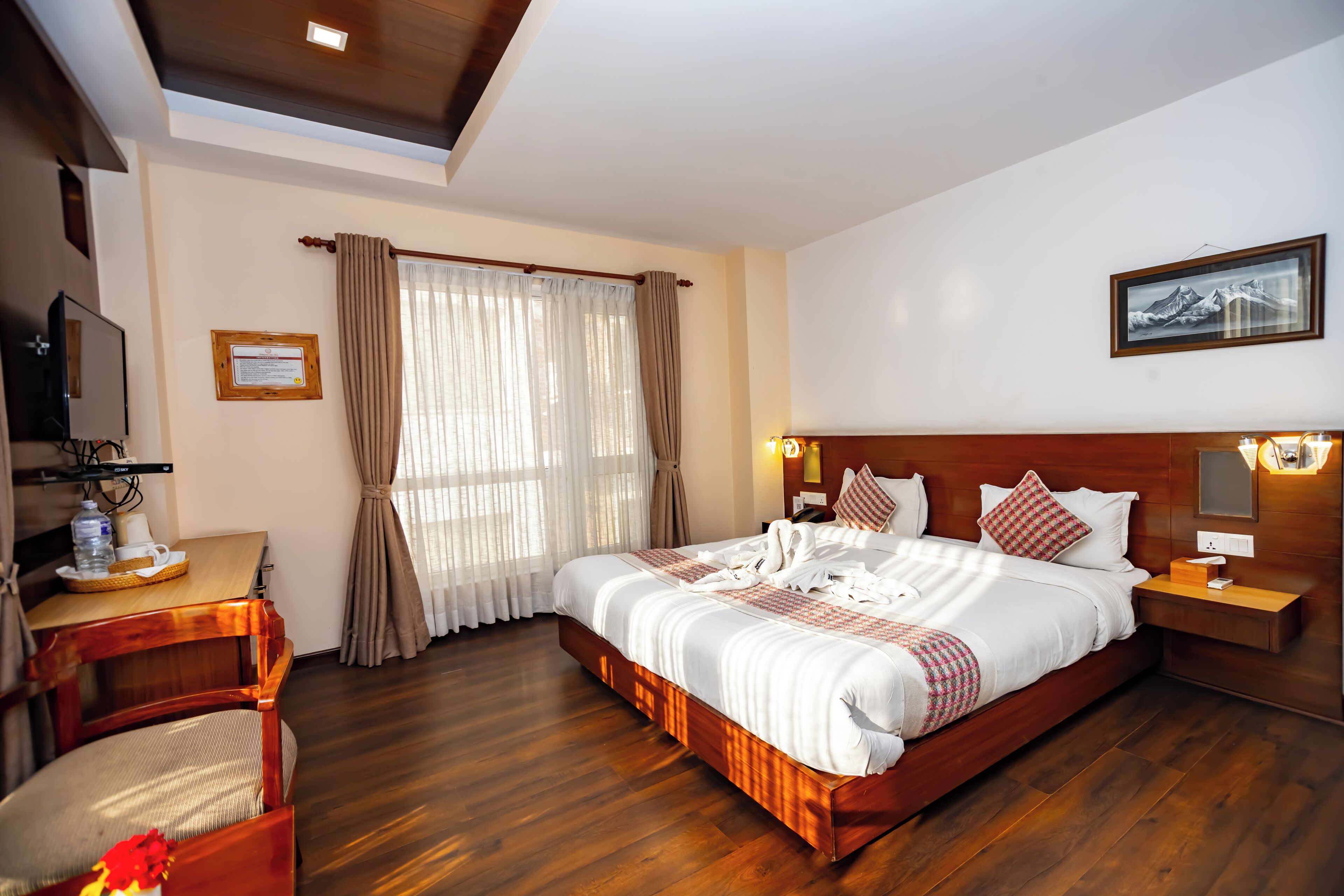 Una habitación de hotel con una cama de madera, un escritorio con una silla, un televisor y un cuadro en la pared.