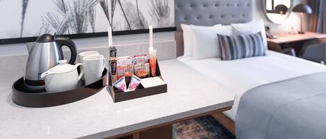 A hotel room with a bed, a bedside table with a lamp, a tray with breakfast items, and a coffee maker.