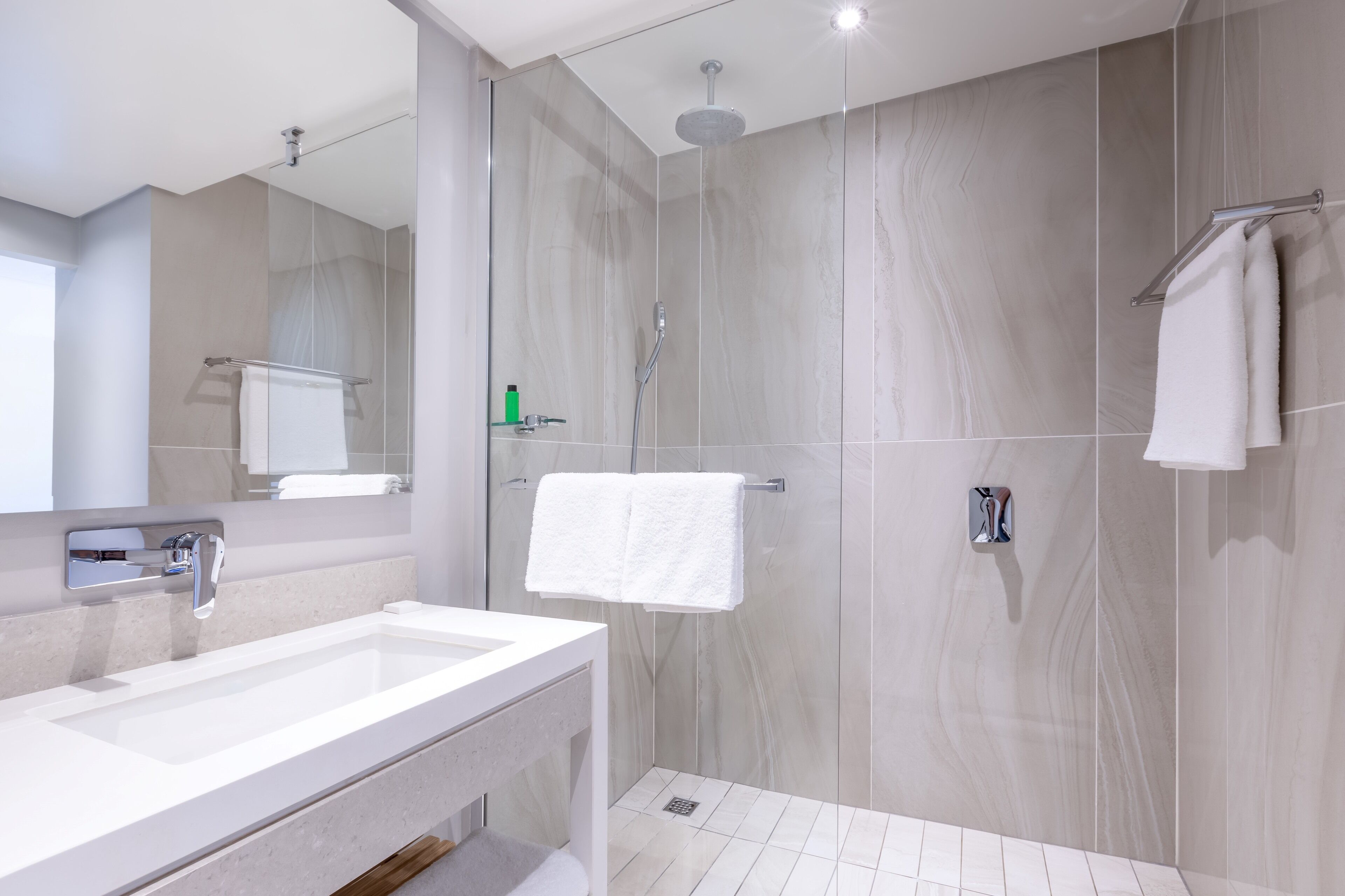 Een moderne badkamer met een grote spiegel, twee wastafels, een douche en een handdoekhouder.