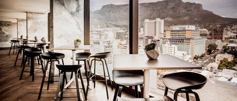 A modern interior with a city view, featuring a wooden floor, black chairs, a table, and a potted plant.
