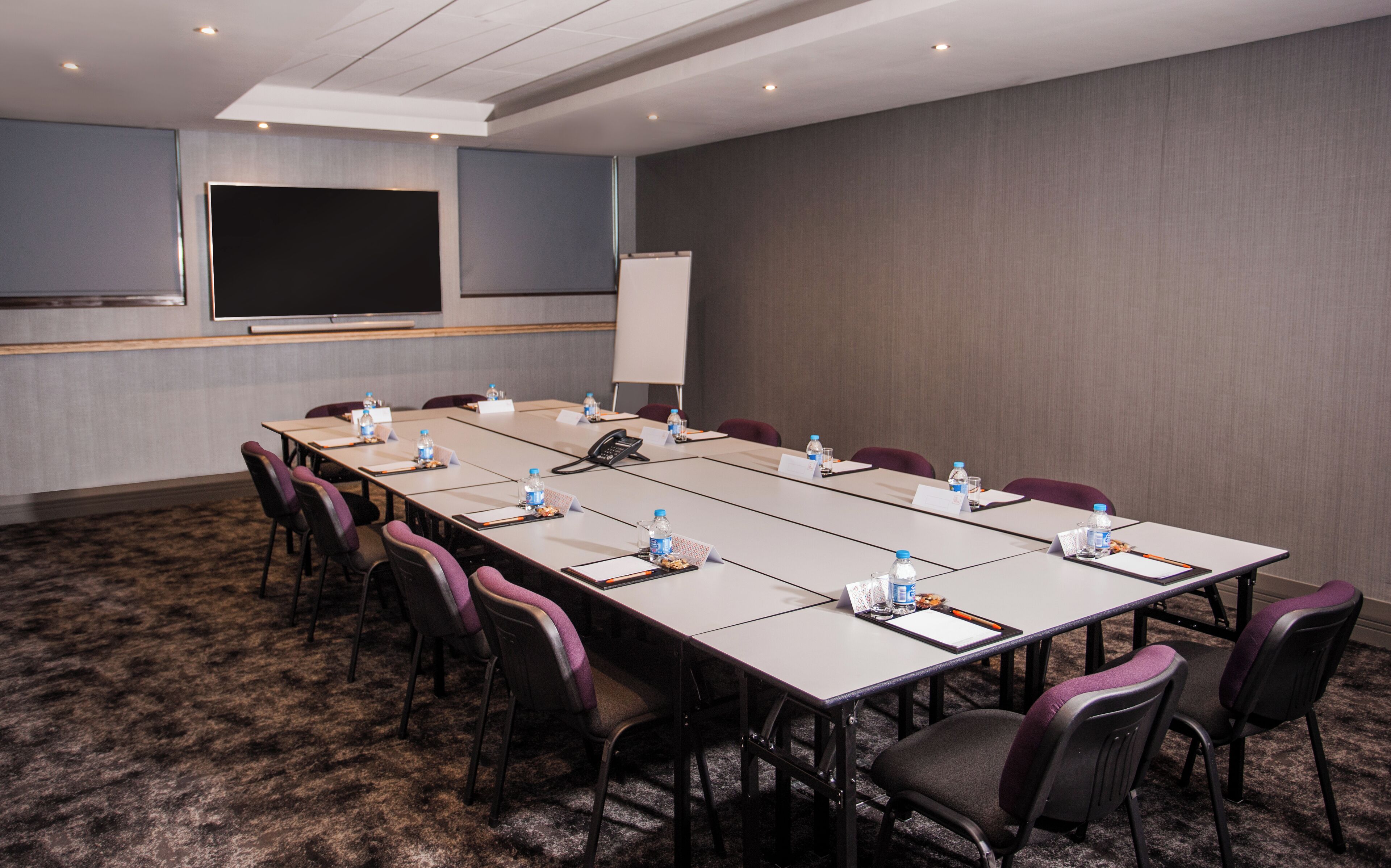 A conference room with a long table, chairs, water bottles, nameplates, and a whiteboard.