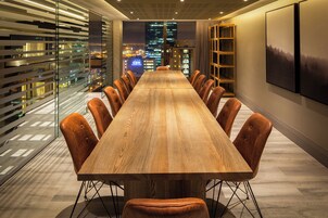 A conference room with a long wooden table, leather chairs, and a city view through large windows.
