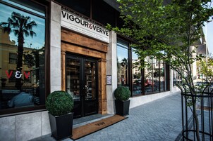 A storefront with a sign reading "VIGOUR & VERVE" and a reflection of palm trees in the window.