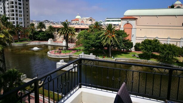 Un balcon avec vue sur une rivière, des palmiers et des bâtiments en arrière-plan.