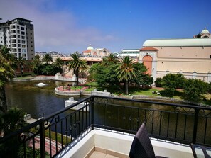 A balcony with a view of a river, palm trees, and buildings in the background. - Island Letting - (Self Catering) The Island Club Apartments (Cape Town)