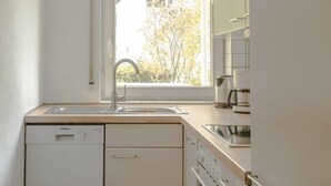 Ett modernt kök med diskmaskin, diskho och ett fönster med utsikt över ett träd.