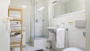 Een moderne badkamer met een douchecabine van glas, een wastafel met spiegel en een handdoekrek met netjes opgevouwen handdoeken.