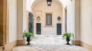 A narrow stone-paved courtyard with two potted plants, a lantern, and a door with a decorative window.