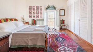A bedroom with two beds, a large window, a radiator, and a patterned rug.