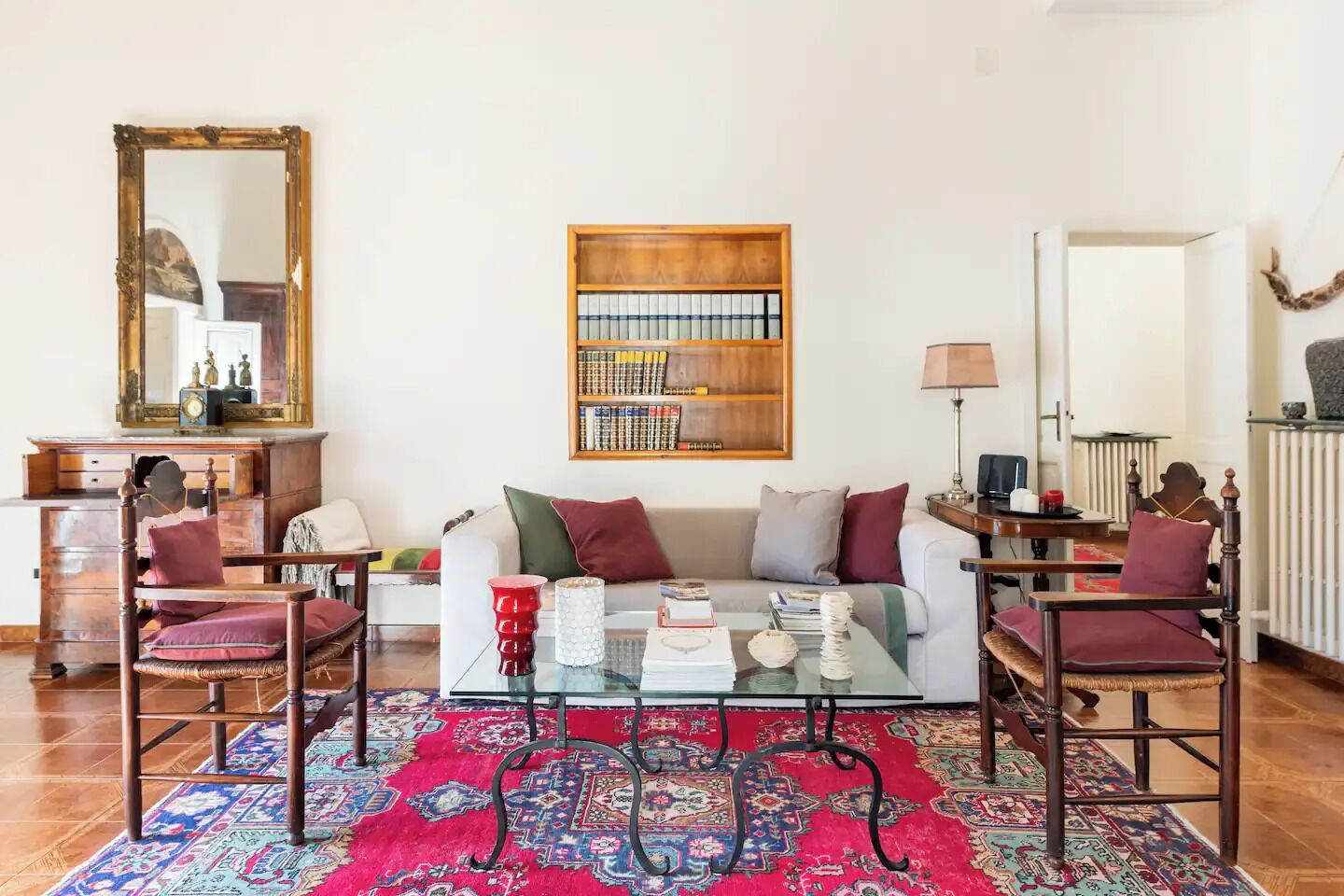 A living room with a sofa, two armchairs, a coffee table, a bookshelf, a mirror, and a radiator.
