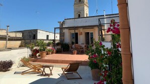 A rooftop terrace with outdoor furniture, potted plants, and a view of a historic tower.