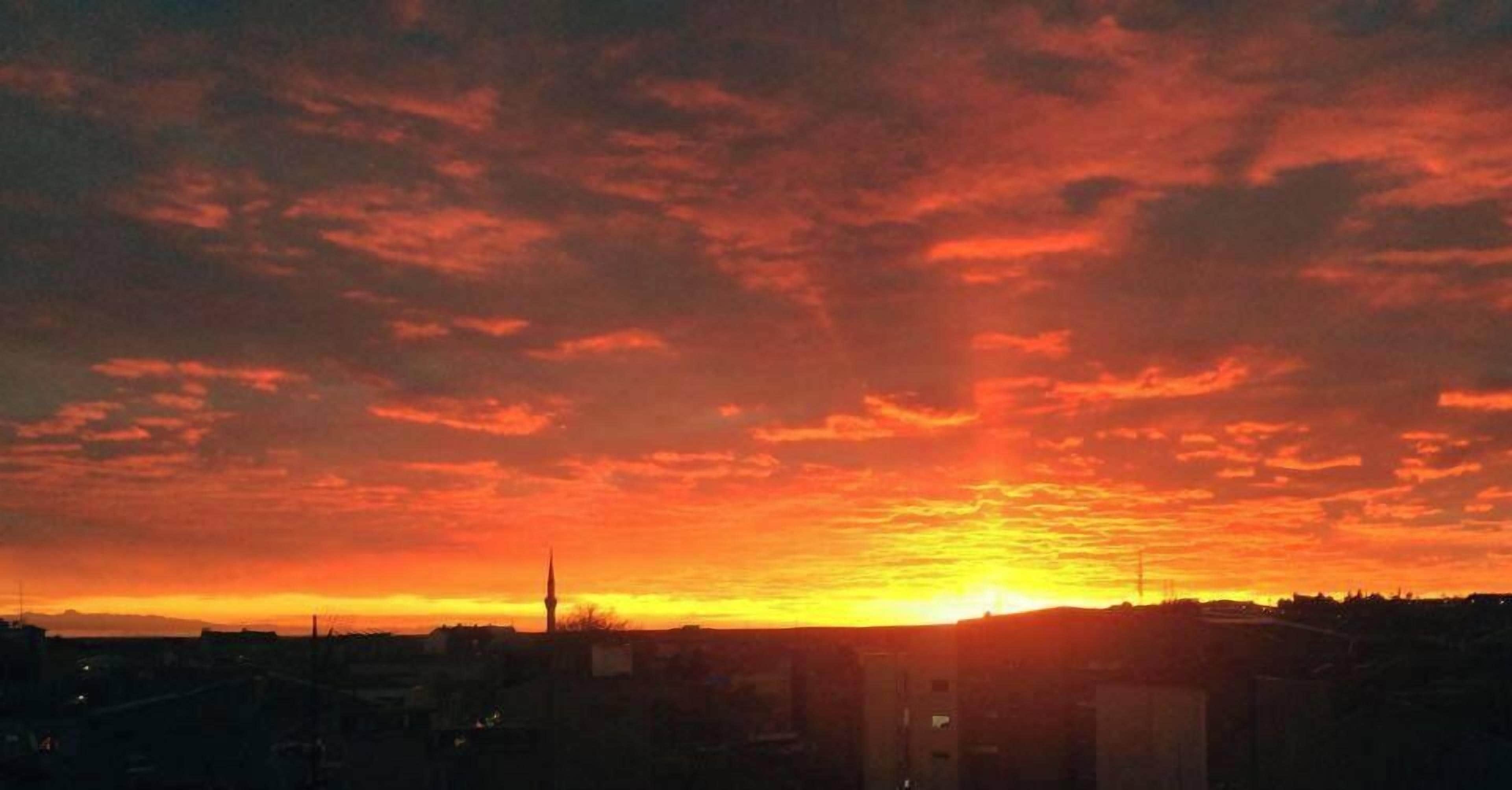 Um pôr do sol sobre a paisagem urbana, com uma torre imponente destacada no céu.