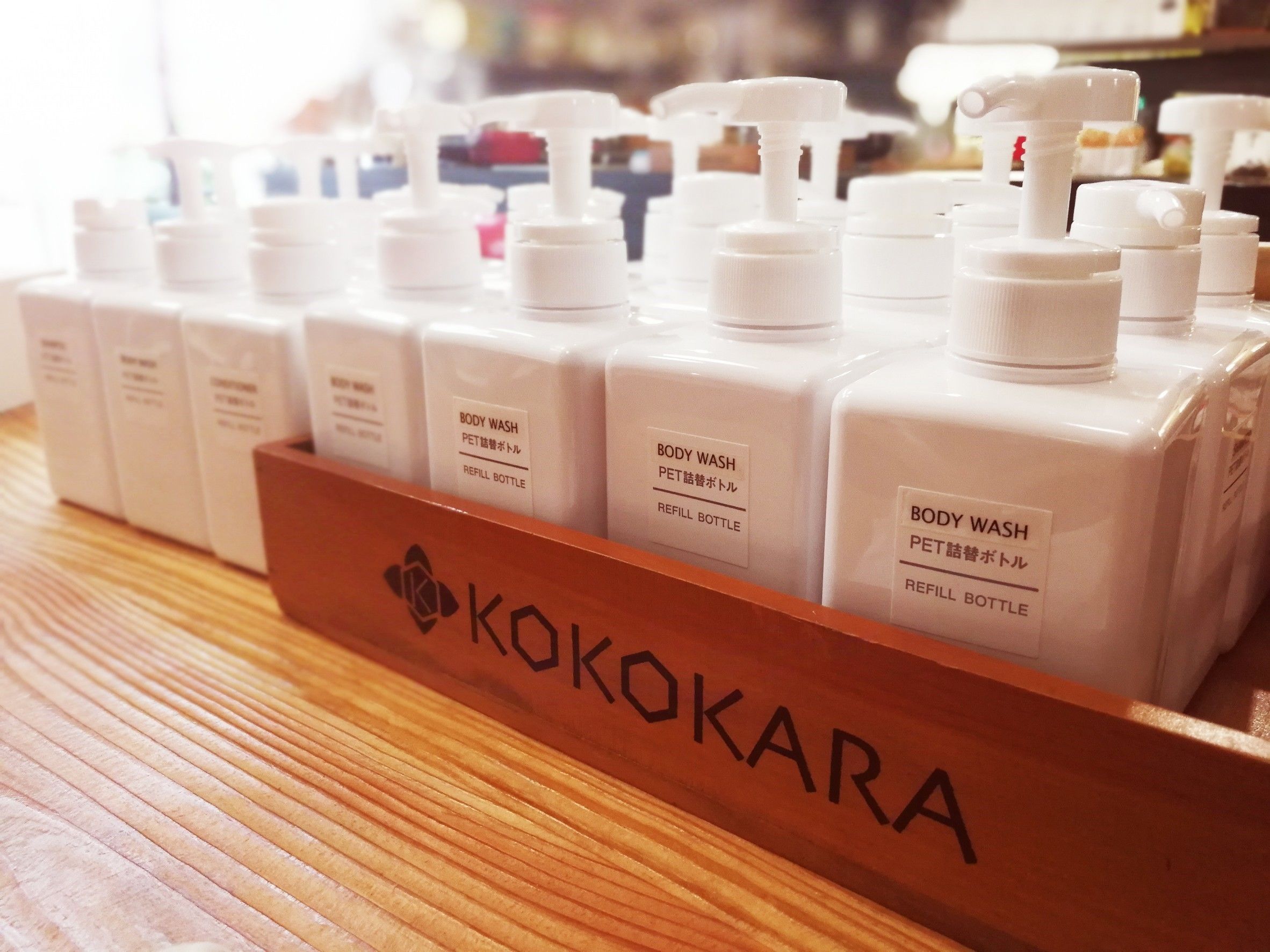 A display of body wash bottles in a wooden case labeled 'KOKOKARA'.