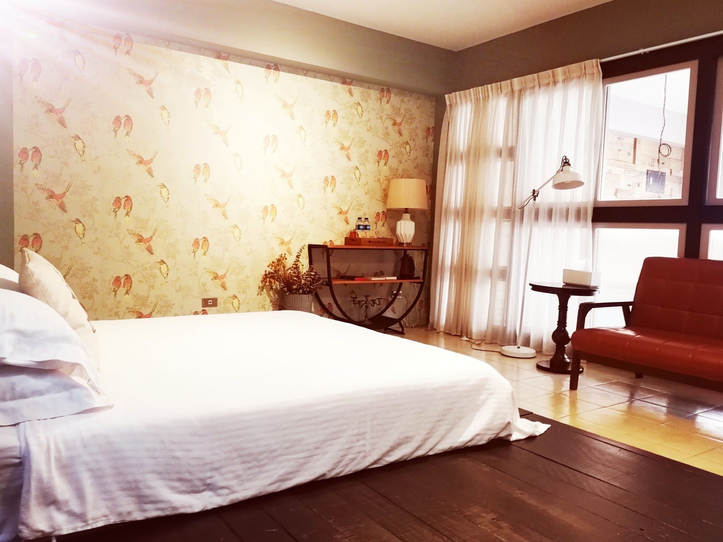 A hotel room with a bed, a desk with a lamp, a chair, and a window with curtains.