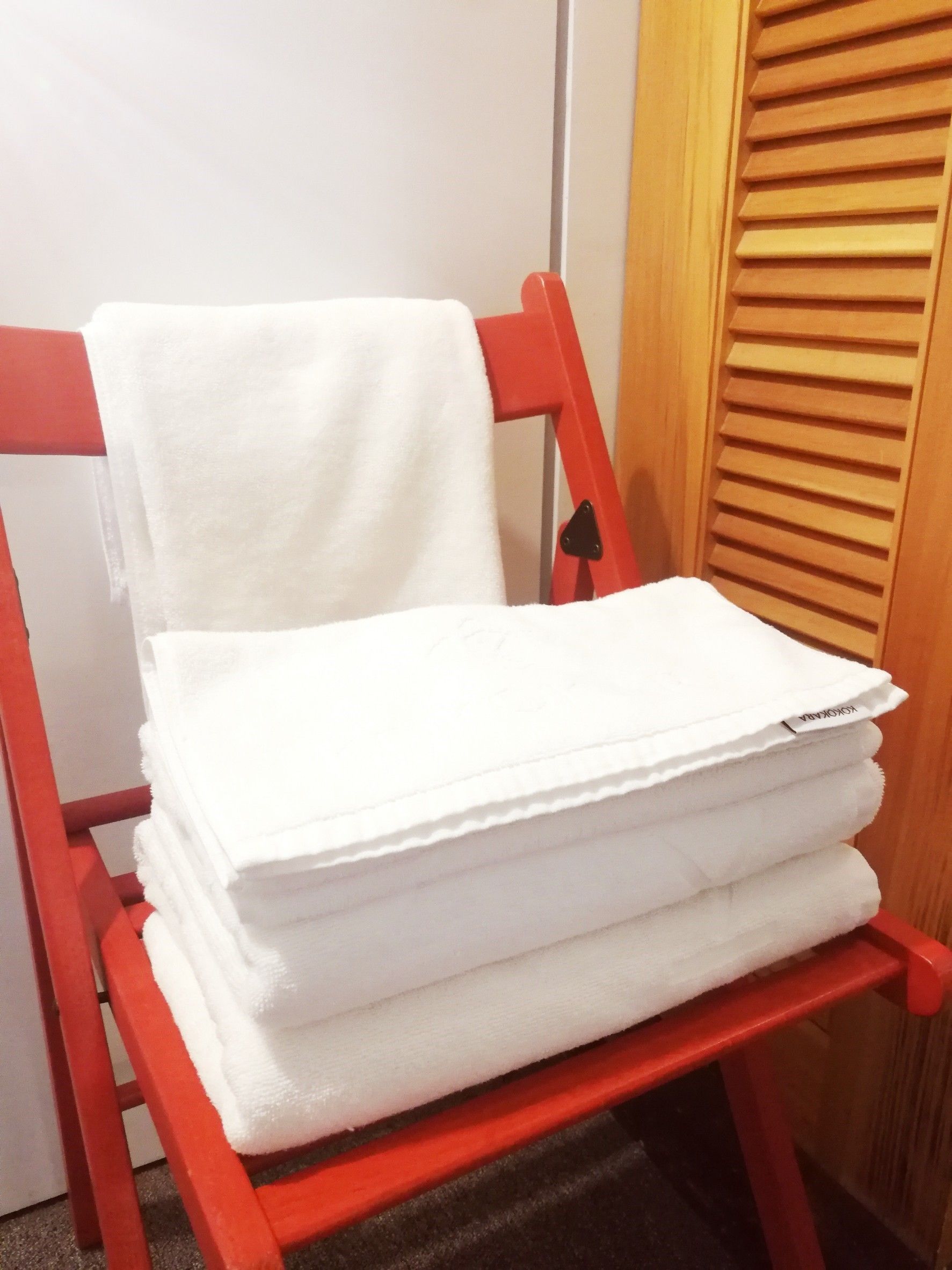 A stack of white towels on a red chair in a room with a wooden door.