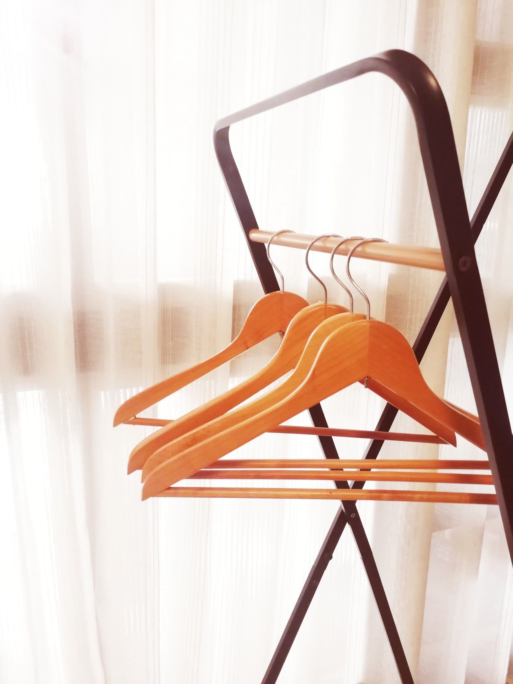 A metal drying rack with wooden hangers against a sheer curtain background.