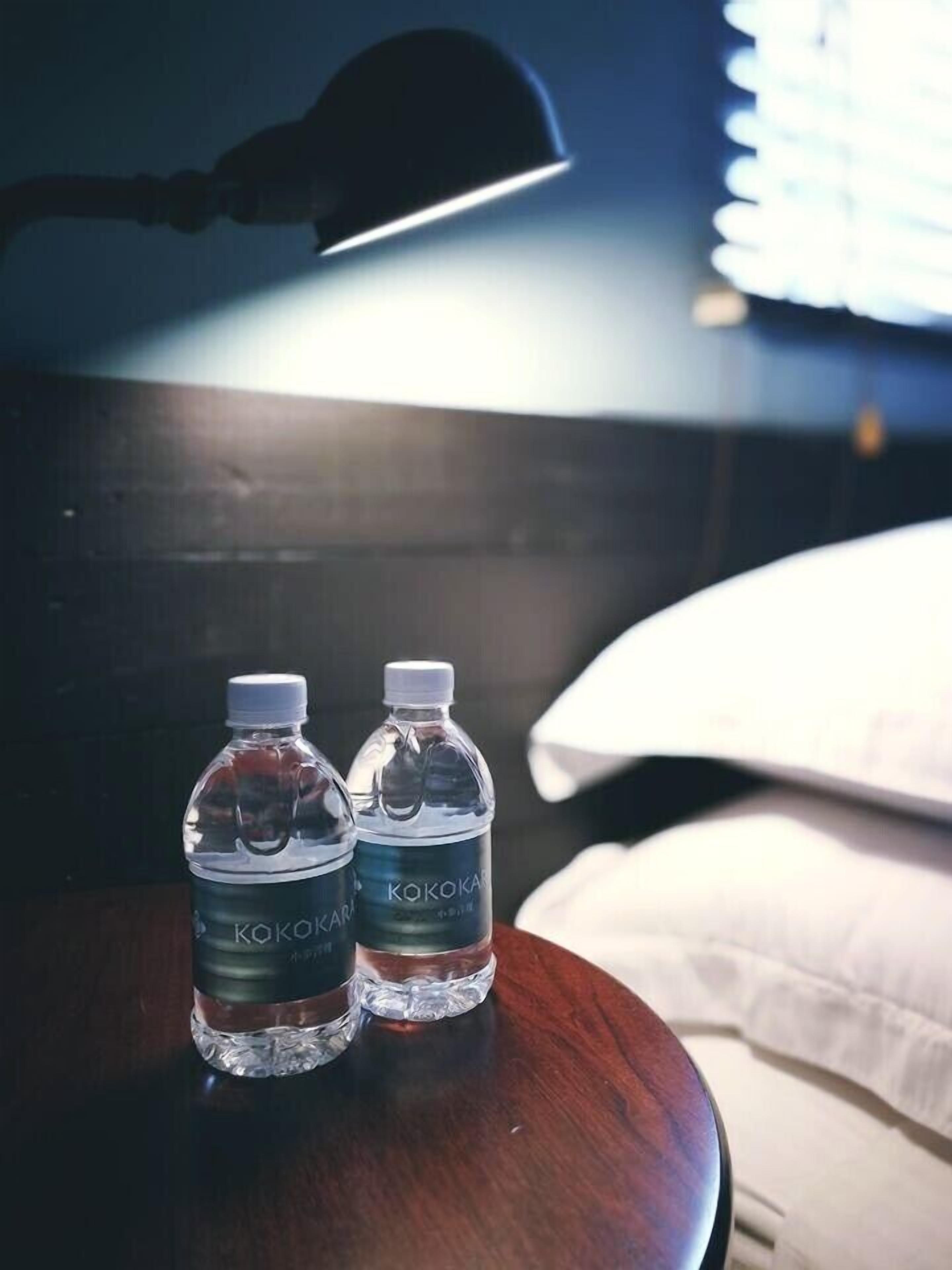 Deux bouteilles d’eau Kokokara sur une table en bois, dans une chambre d’hôtel. On aperçoit une lampe et un oreiller à l’arrière-plan.