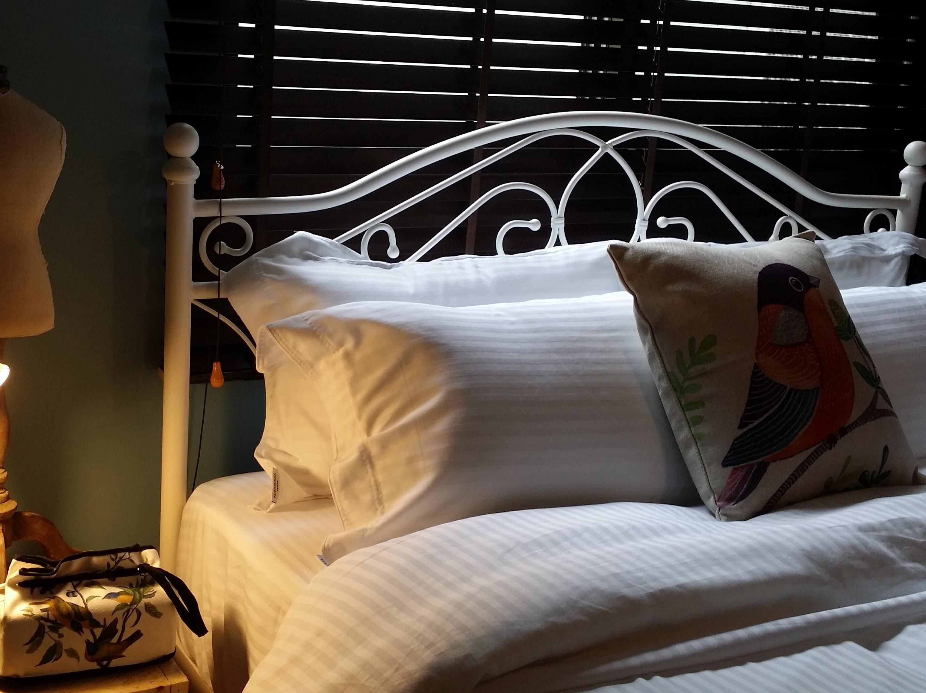 A neatly made bed with white linens and a decorative pillow featuring a bird.