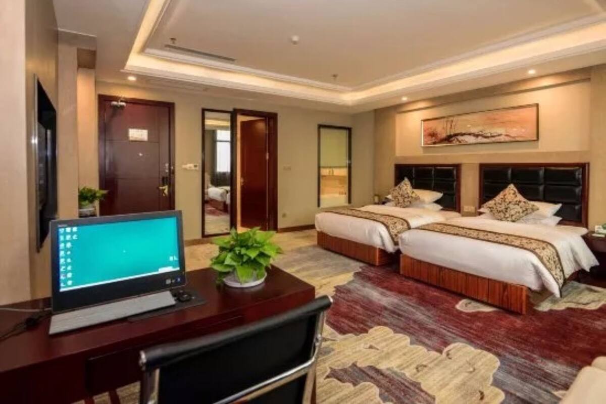 A hotel room with two beds, a desk with a computer, and a large mirror.