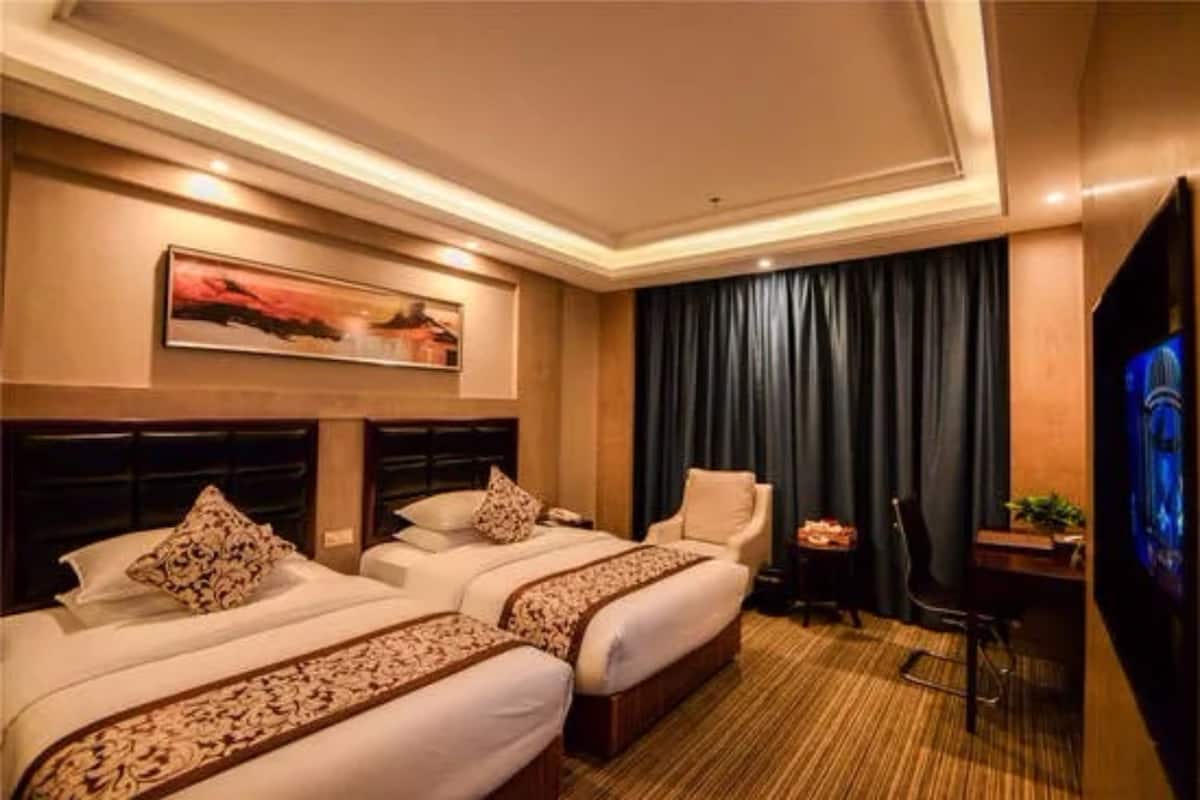 A hotel room with two beds, a desk, a chair, a television, and a painting on the wall.
