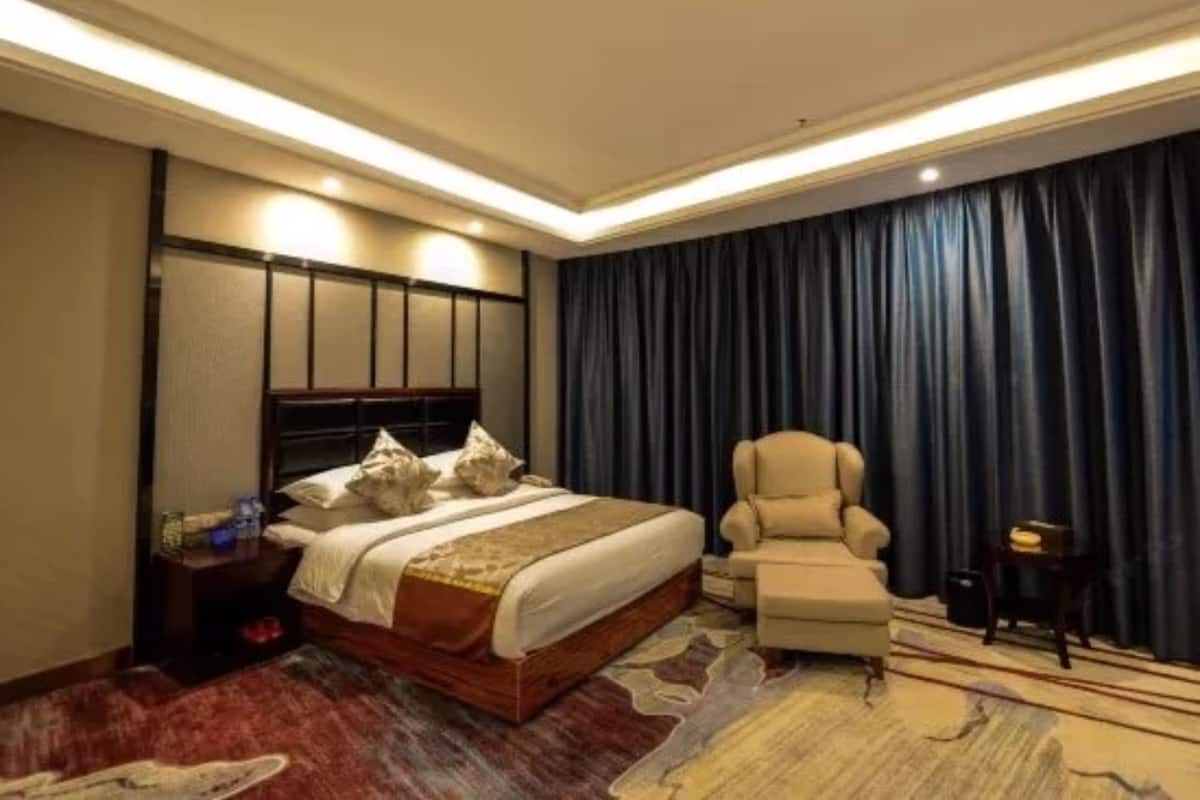 A hotel room with a large bed, a chair, a small table, and a dark curtain.