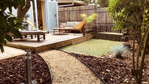 Un giardino con un patio in legno, un'amaca, un divano e un tavolino.
