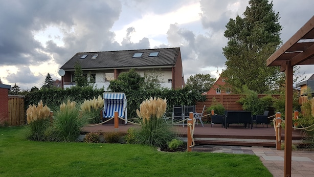 A residential backyard with a grassy lawn, a blue and white striped chair, and a patio area with outdoor furniture.