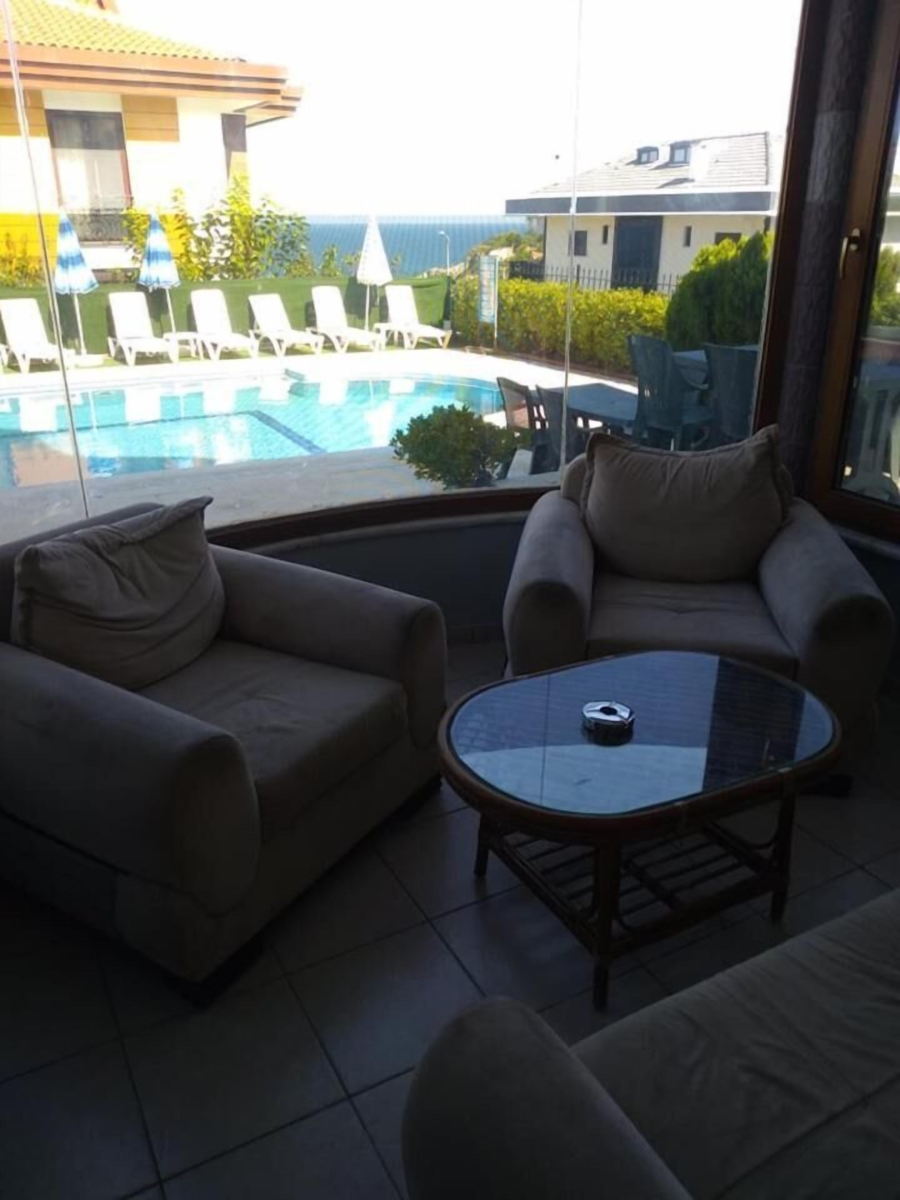 Un balcón con dos sofás y una mesa de vidrio, con vistas a una piscina y a edificios y vegetación.