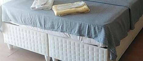 Una cama bien tendida con un edredón gris y blanco, una almohada blanca y una toalla doblada en el reposapiés.