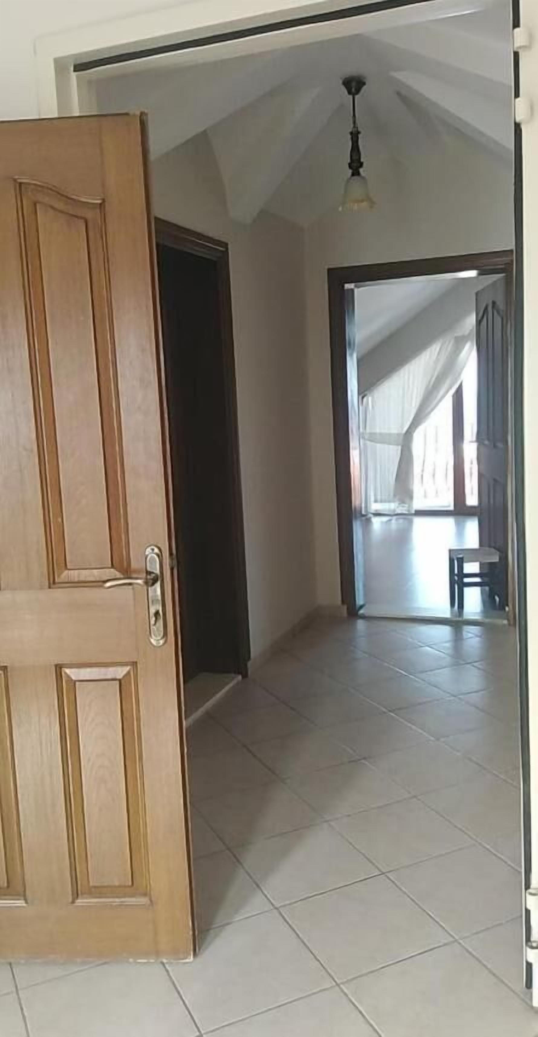 Una porta in legno aperta che dà su una stanza con pavimento in piastrelle e ventilatore a soffitto.