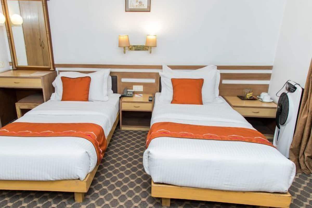 A hotel room with two single beds, a wooden headboard, a nightstand with a lamp, a mirror, and a small table with a fan.