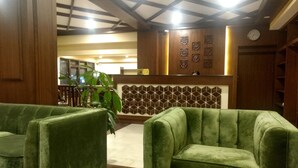 Un vestíbulo con sofás tapizados en verde, un mostrador de recepción y una pared decorativa con patrones geométricos.