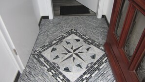 Um corredor com piso estampado, um rodapé de porta e um tapete de entrada.