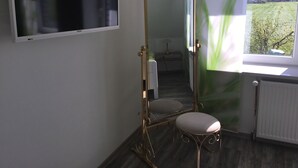 Quarto com um espelho grande, televisão fixada na parede, radiador e janela com vista para o verde lá fora.