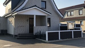 Uma casa moderna de dois andares com um telhado empenaço proeminente, varanda frontal e uma pequena garagem anexa.