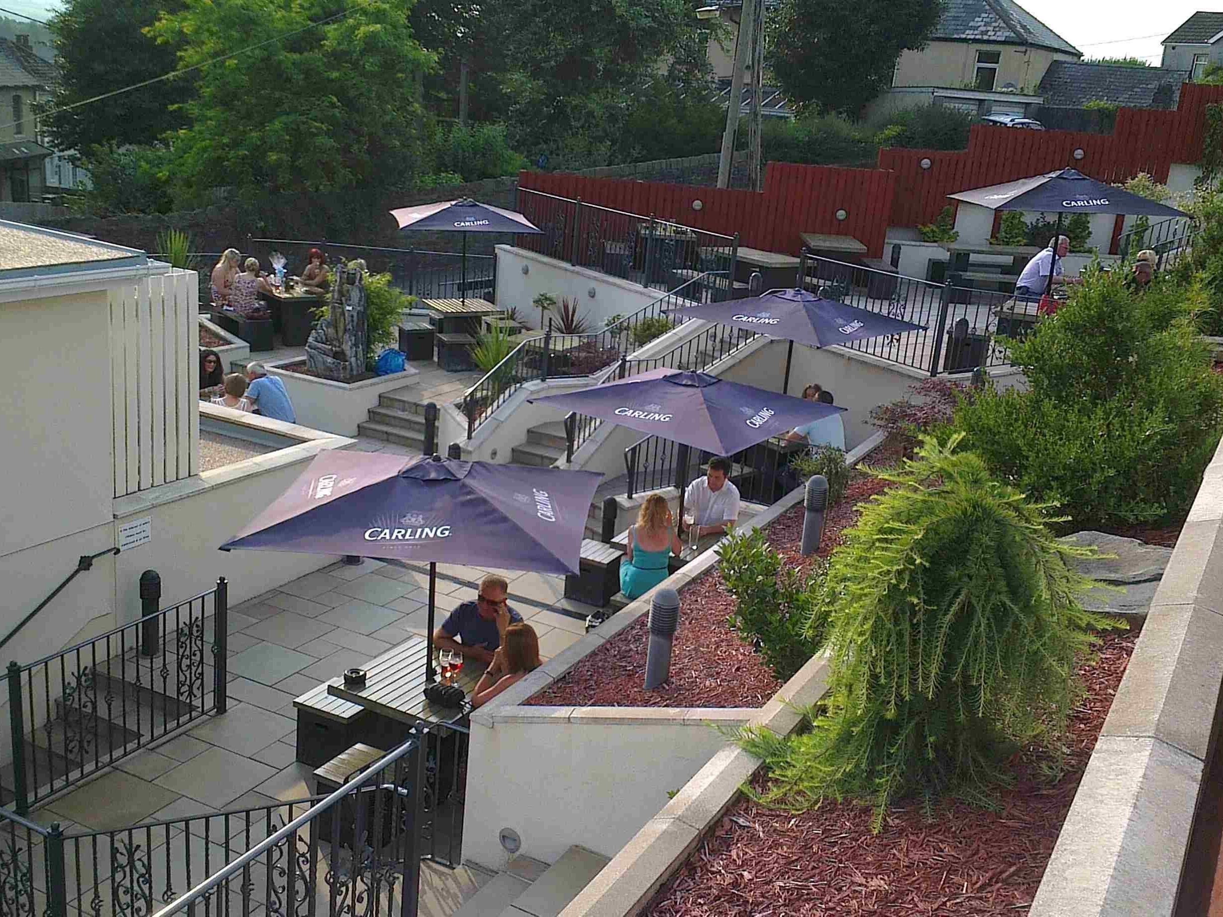Una terraza en la azotea con mobiliario exterior, cubierta por sombrillas 'Carlings', y una escalera que conduce a un nivel superior.