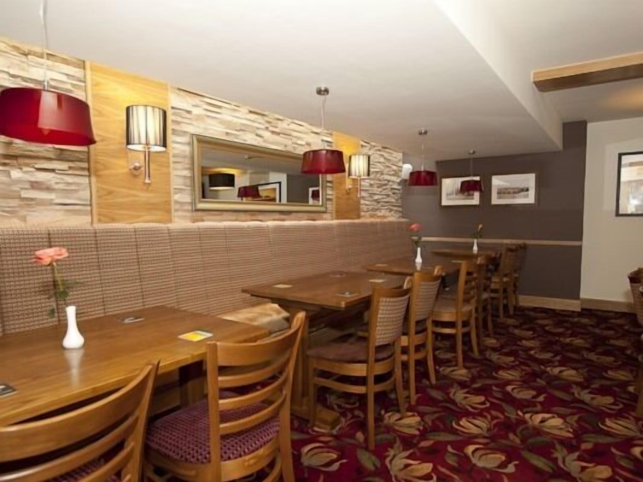 Un restaurante con mesas y sillas de madera, decoración de pared de piedra y lámparas colgantes rojas.