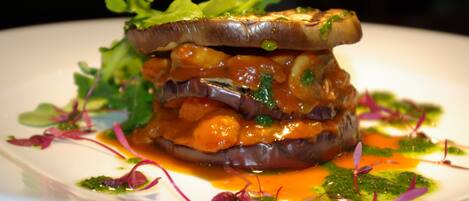 A dish with a slice of eggplant and greens on top, surrounded by sauce and greens.
