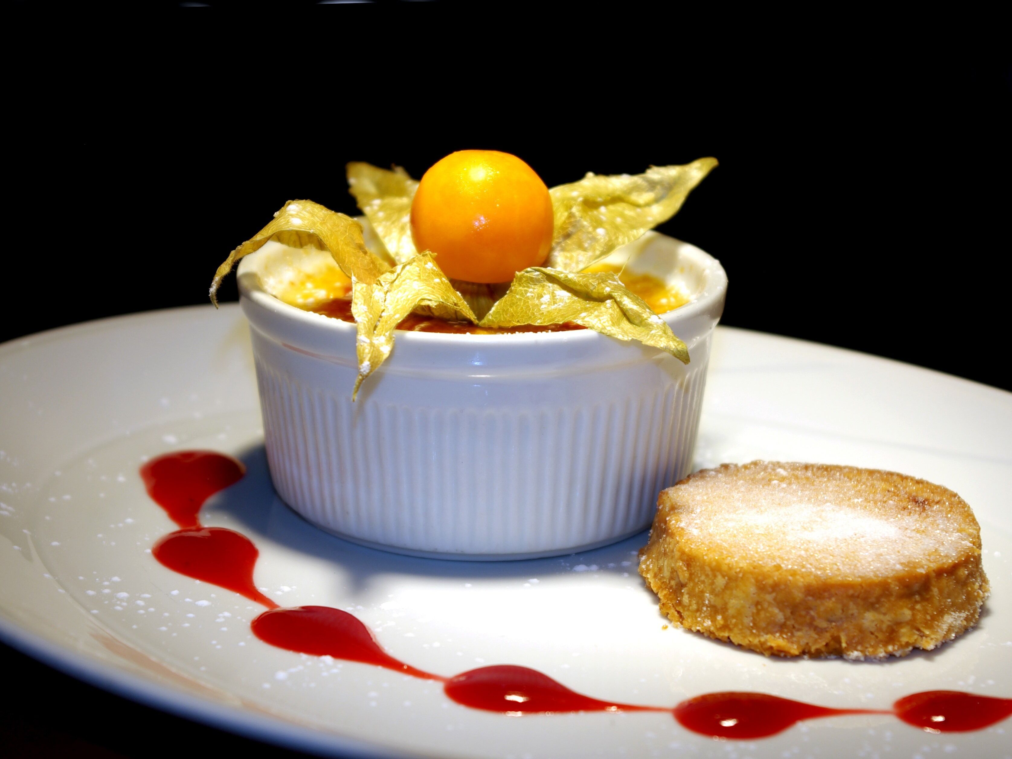 A dessert in a white ramekin on a plate with a red sauce design.