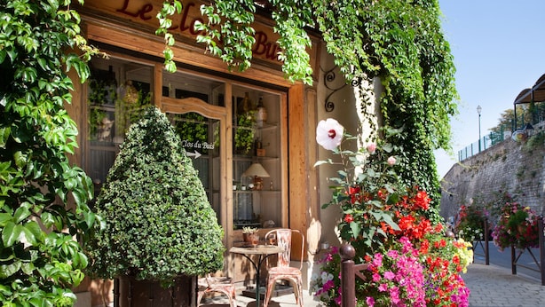Un rincón exterior acogedor con una mesa y sillas, rodeado de abundante follaje y flores vibrantes.
