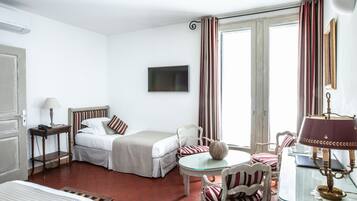 Una habitación de hotel con cama, escritorio con lámpara, silla, televisión y ventana con cortinas.