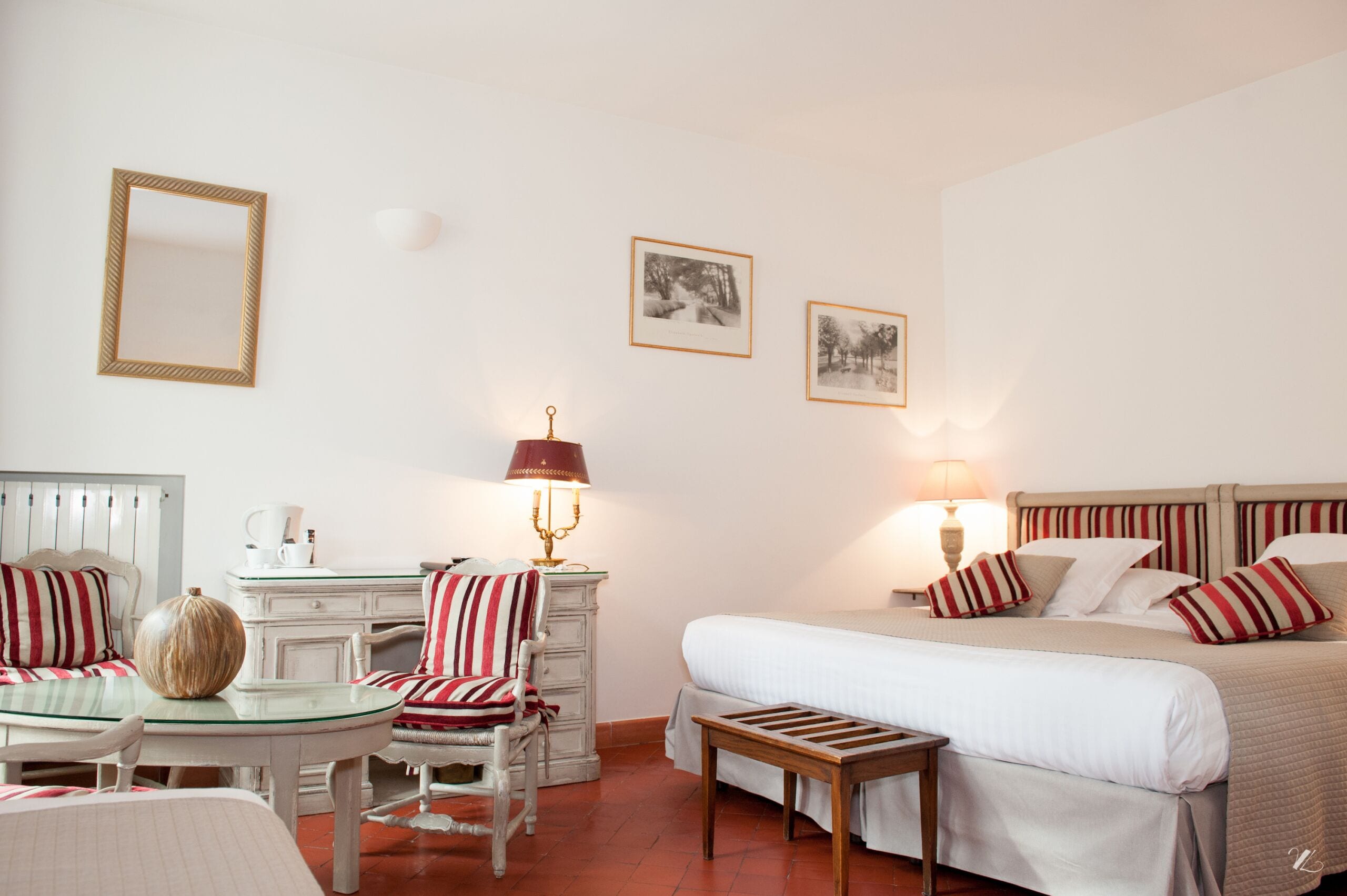 Habitación de hotel con cama, escritorio, silla, lámpara y dos cuadros en la pared.