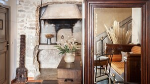 Un interior rústico con pared de piedra, chimenea, banca de madera y un jarrón con flores.